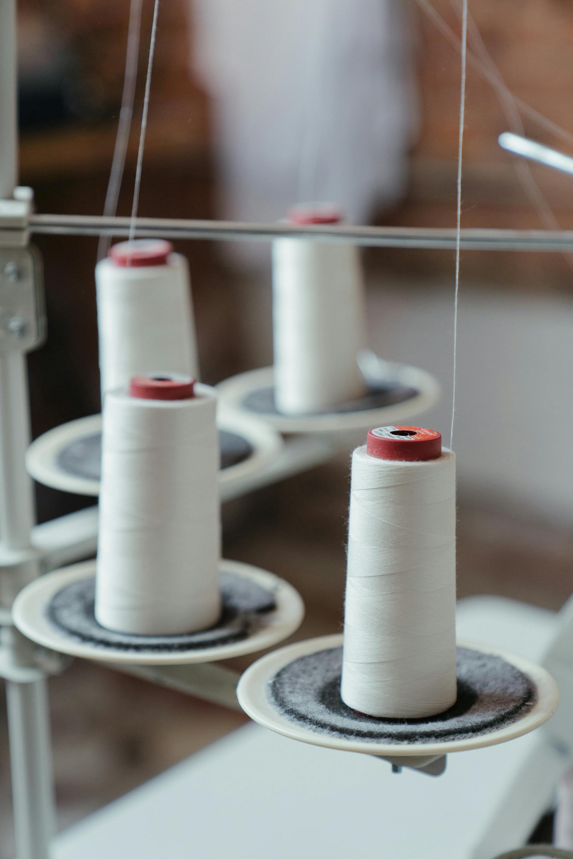 White yarn rolls of yarn mounted onto a sewing machine.